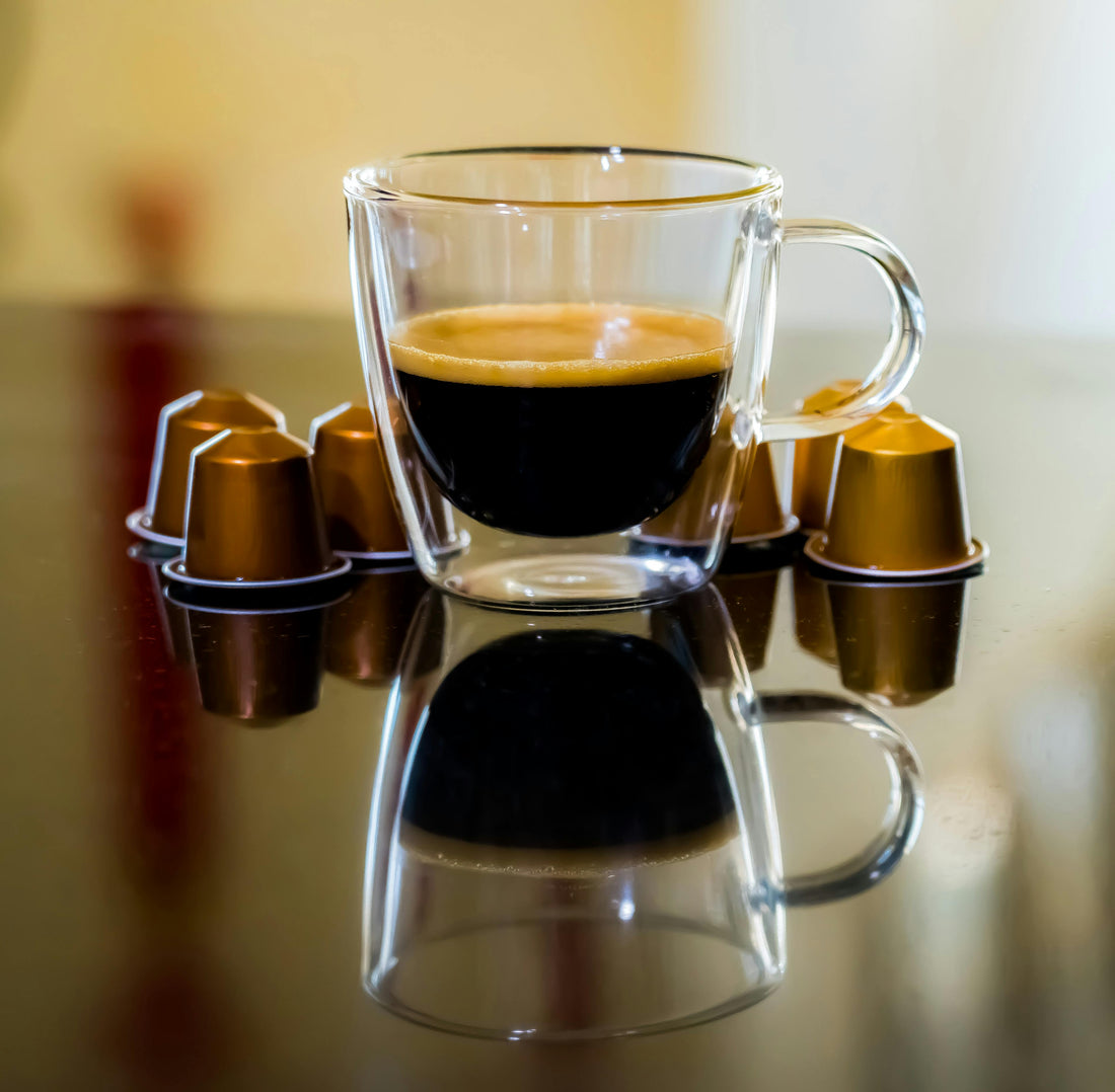 A rich cup of coffee sitting on a dark wood table next to k-pods