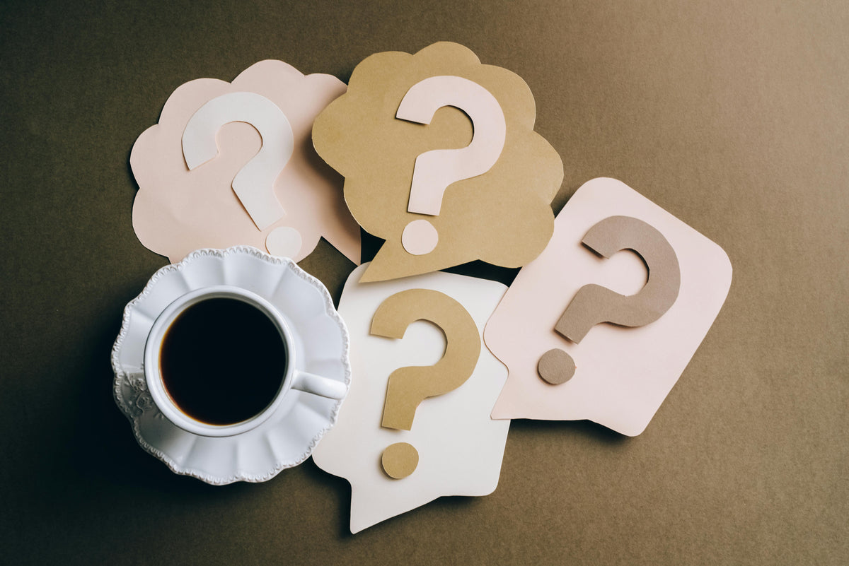 Cardboard cutouts of question marks with a cup of coffee on a brown background
