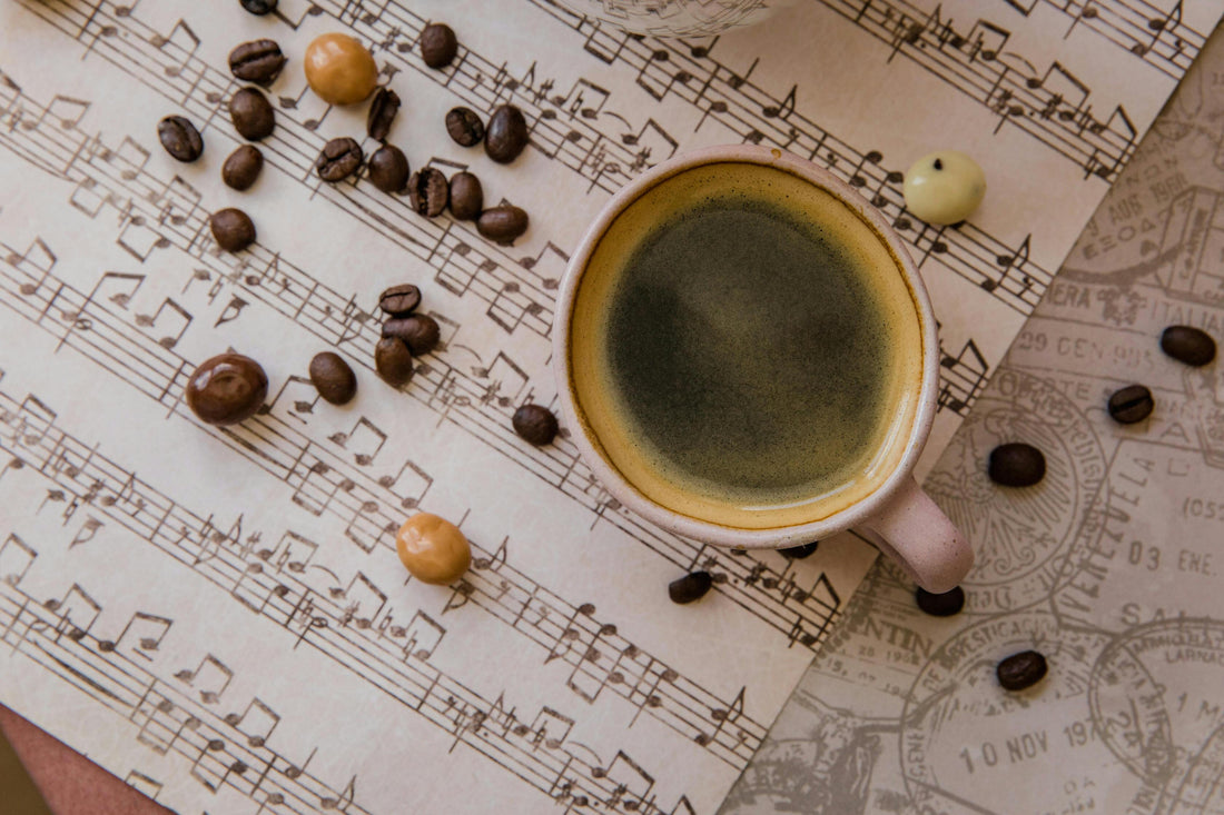A cup of coffee sitting on sheets of music with chocolate and coffee beans expressing flavor notes