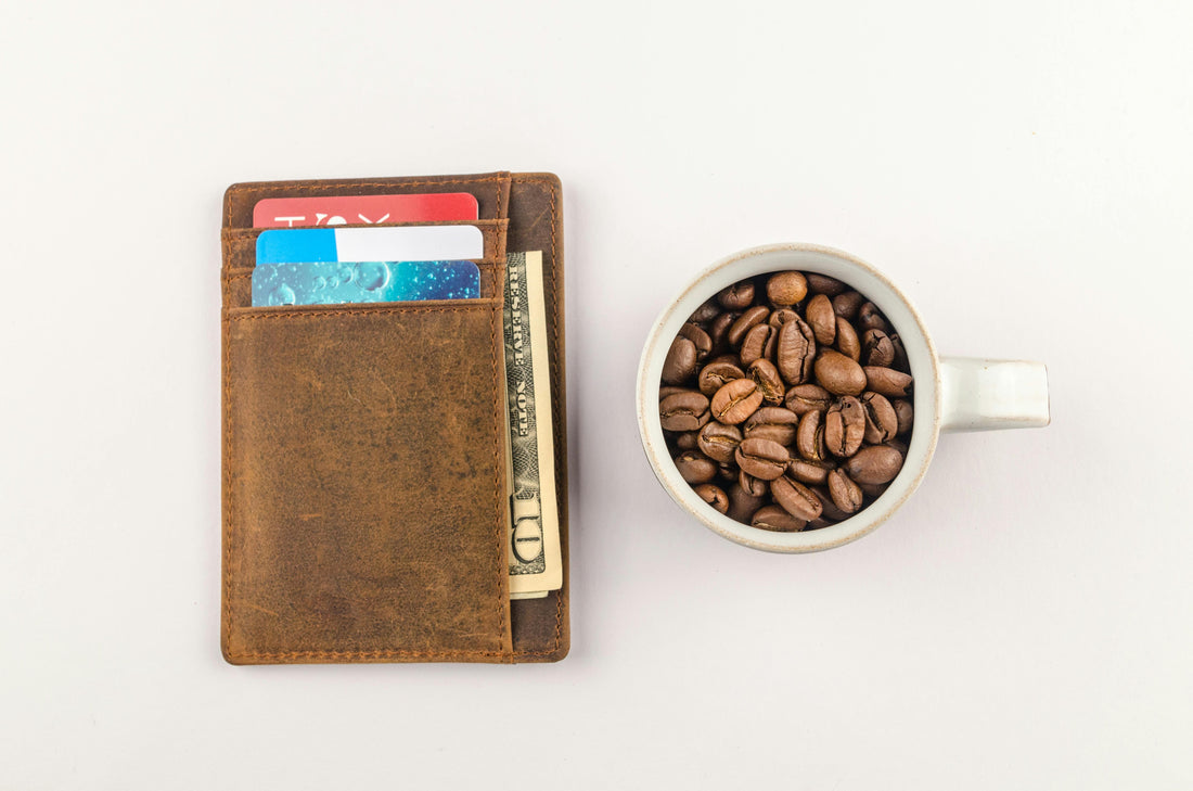 Brown leather wallet with cards and a bill next to a cup filled with coffee beans on a white background
