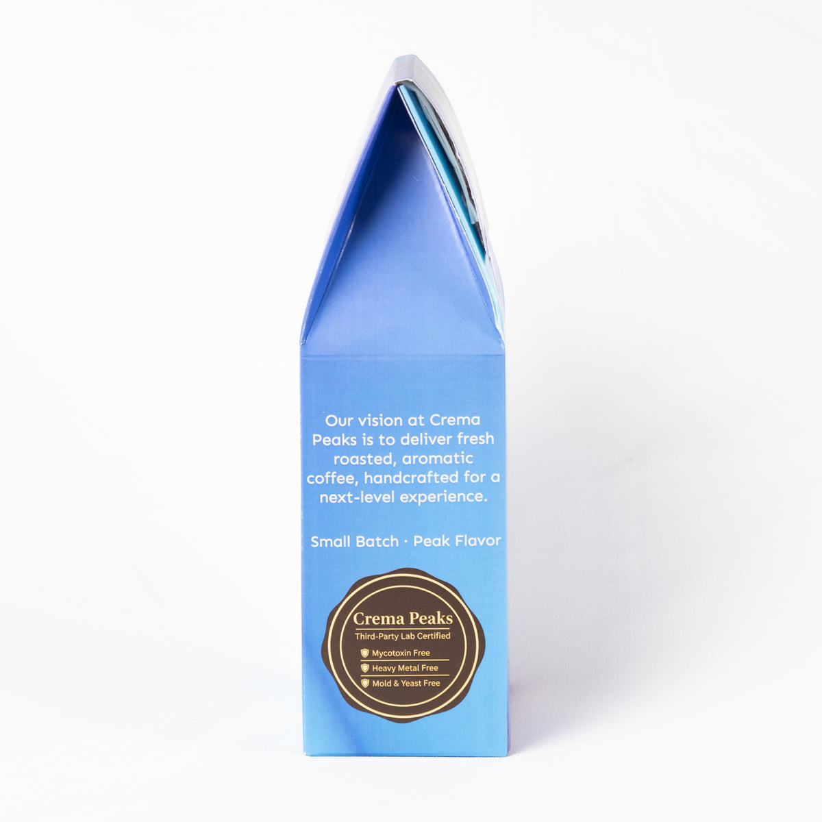 A tall, narrow blue coffee gift box with a pointed top, photographed on a clean white background. The front features white text and a circular gold and black logo for Crema Peaks.