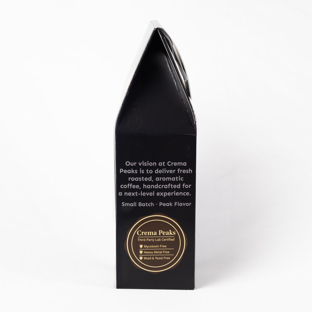A tall, black coffee bag package standing upright on a white background. The front features white descriptive text and a circular gold logo for Crema Peaks.