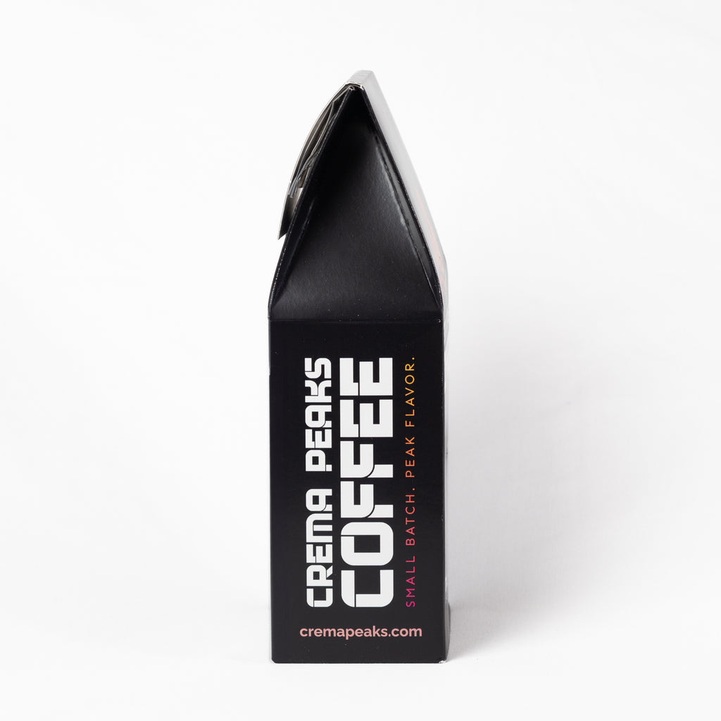 A black coffee bag package shown upright against a clean white background, with large white vertical text reading 'CREMA PEAKS COFFEE' and smaller pink text reading 'SMALL BATCH, PEAK FLAVOR.'.