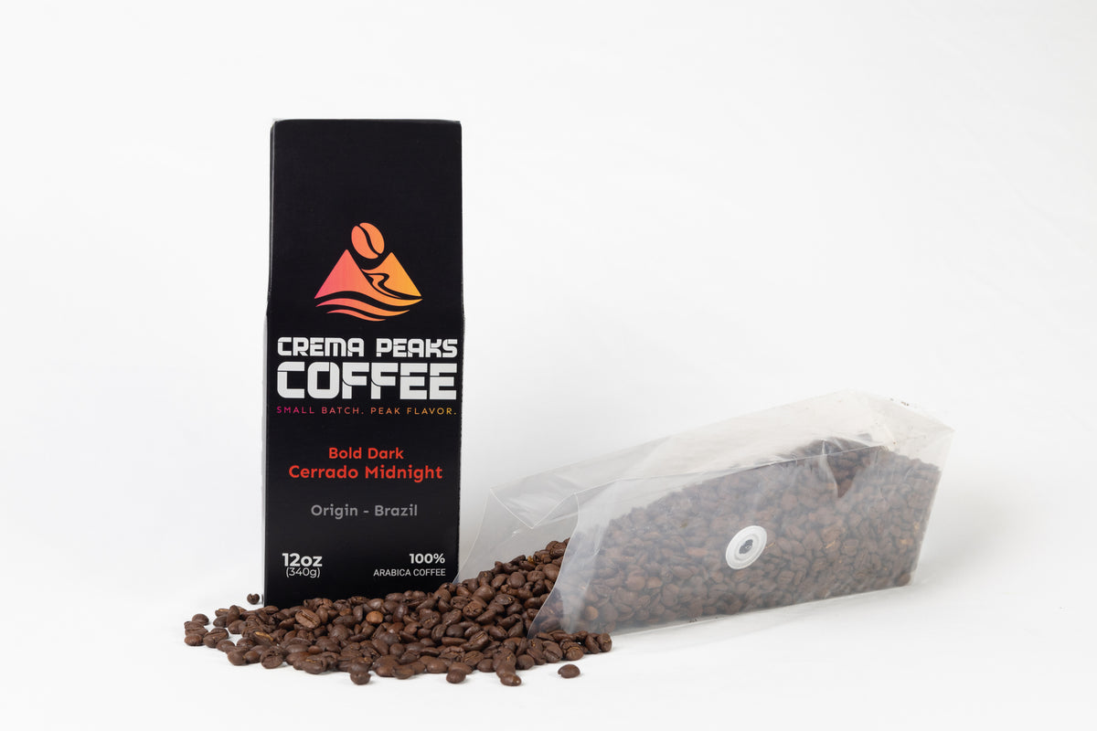 Crema Peaks Coffee Bold Dark Cerrado Midnight coffee packaging shown with a black branded bag standing upright and a clear plastic bag of coffee beans lying on its side with coffee beans spilled in front, on a white studio background.