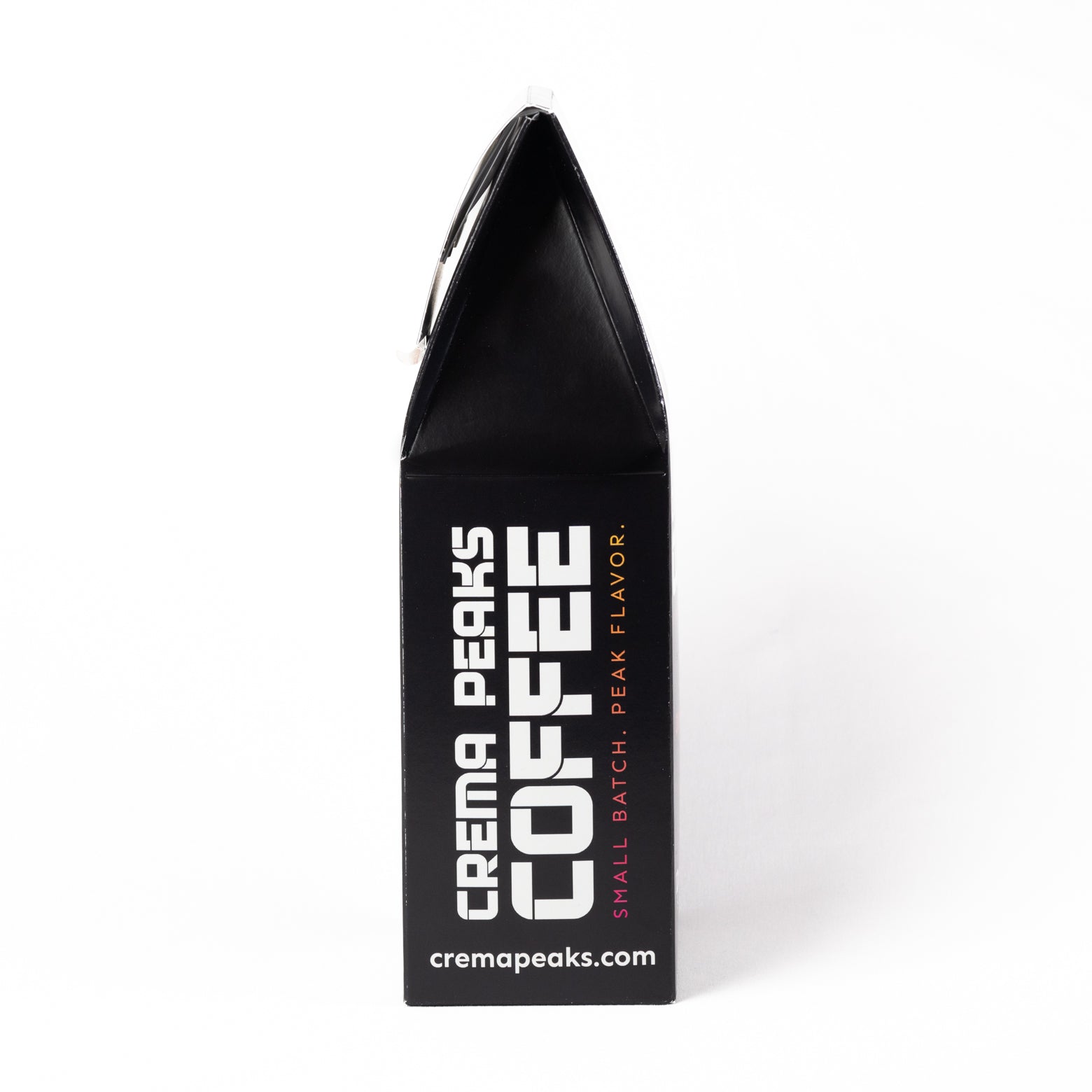 A black coffee bag package from Crema Peaks Coffee, standing upright on a white background. The packaging features bold white text reading 'CREMA PEAKS COFFEE' and smaller pink text reading 'SMALL BATCH, PEAK FLAVOR.