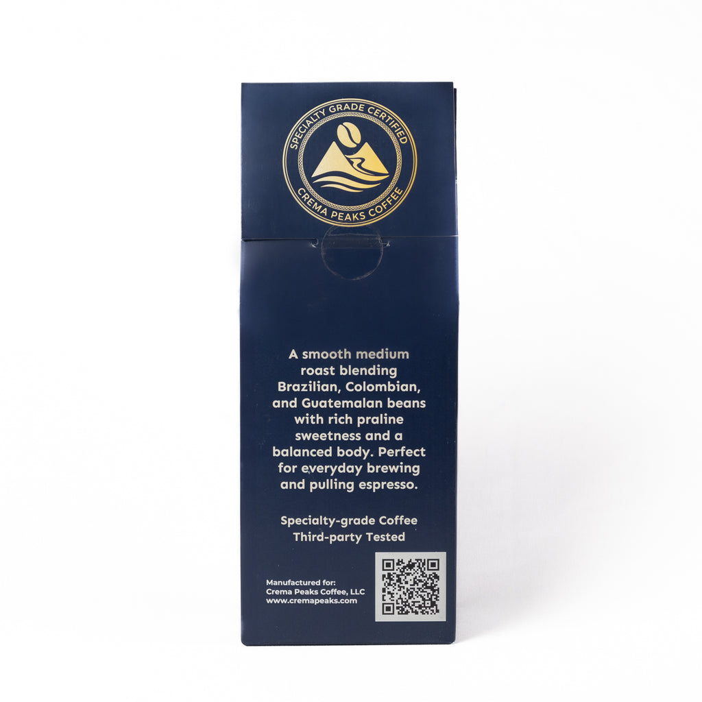 A tall, dark blue coffee bag package shown upright on a white background. The front features a circular gold and white logo for 'Specialty-grade Coffee' and white text describing a smooth medium roast coffee blend from Brazil, Colombia, and Guatemala.