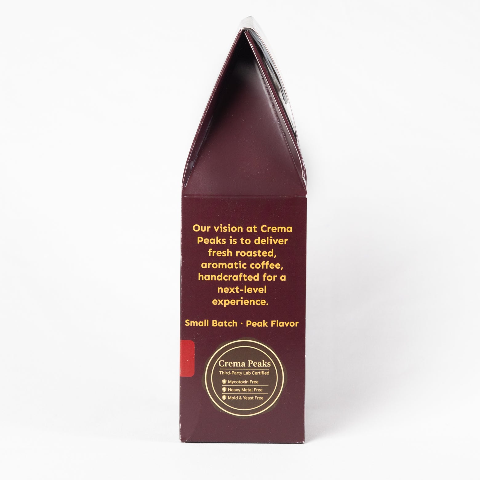 A tall, narrow cream-colored paperboard box for Crema Peaks coffee, shown from the back side against a plain white background. The box is dark maroon-brown with gold text and a circular gold logo at the bottom.