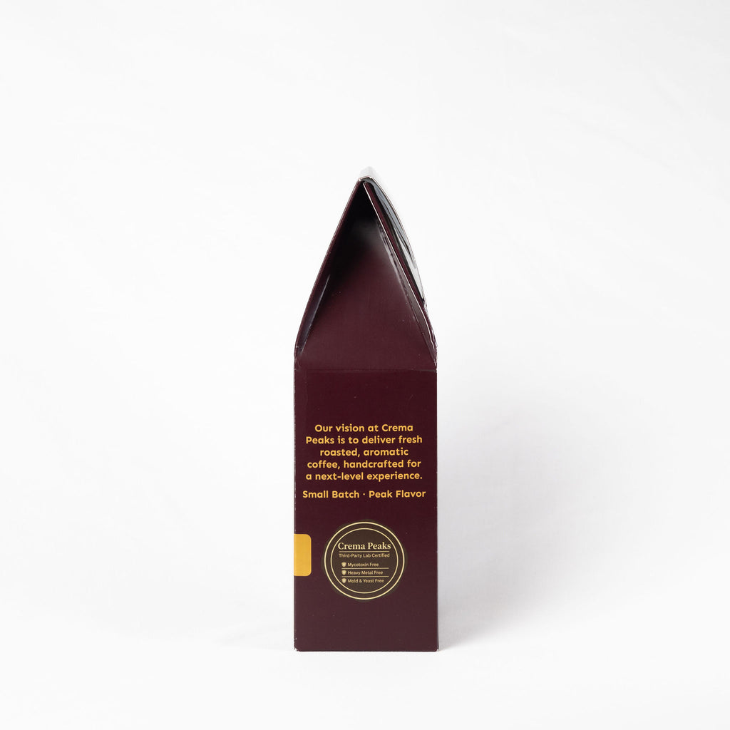 A tall, narrow dark burgundy coffee bag package standing upright on a clean white background. The front features gold text and a circular gold logo for Crema Peaks.