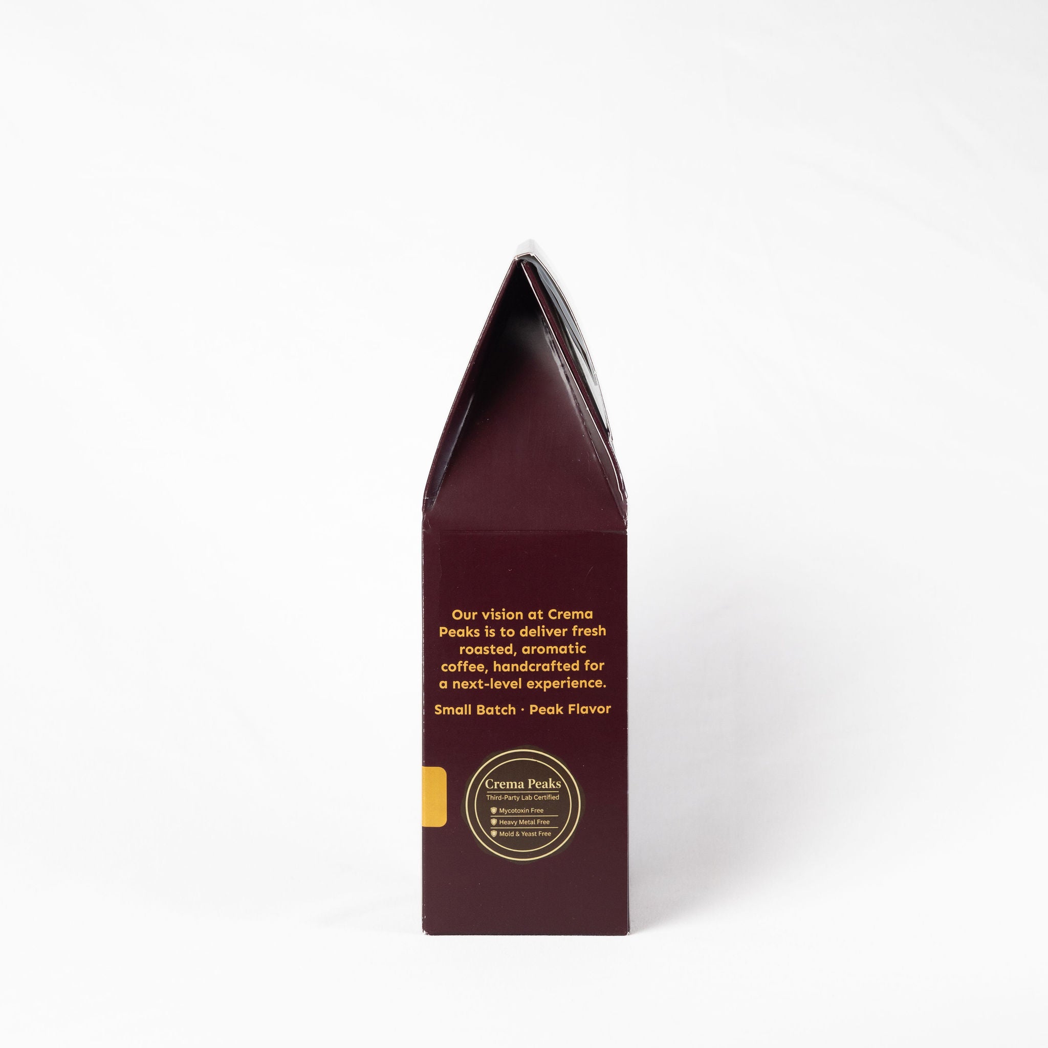 A tall, narrow dark burgundy coffee bag package standing upright on a clean white background. The front features gold text and a circular gold logo for Crema Peaks.