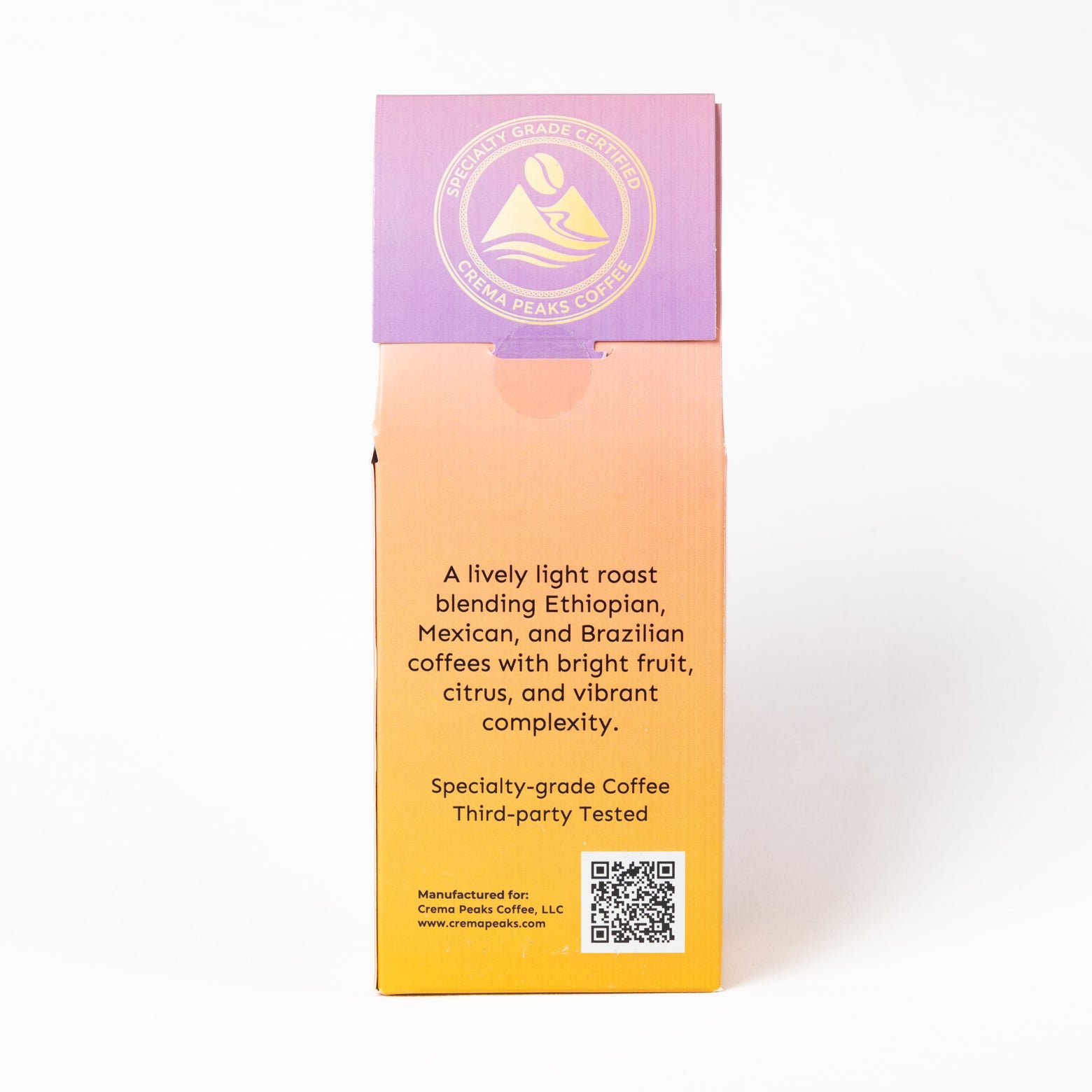 A tall rectangular coffee box shown upright on a clean white background. The packaging has a purple-to-orange gradient front with black product description text and a gold circular logo near the top, plus a QR code at the lower right.
