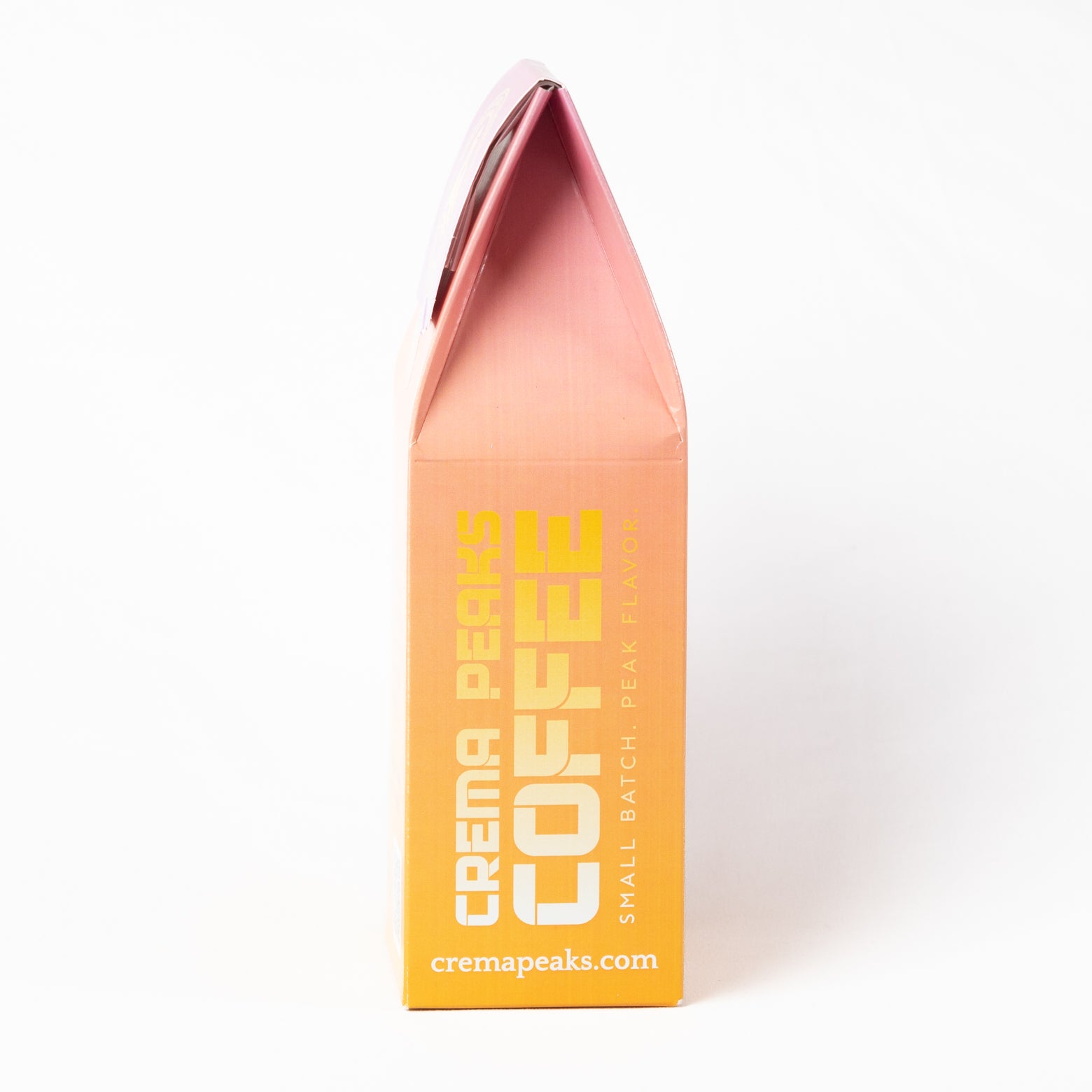 A small triangular paper coffee bag package standing upright on a white background. The package has a pink-to-orange gradient design with bold yellow text reading 'CREMA PEAKS COFFEE' and 'cremapeaks.