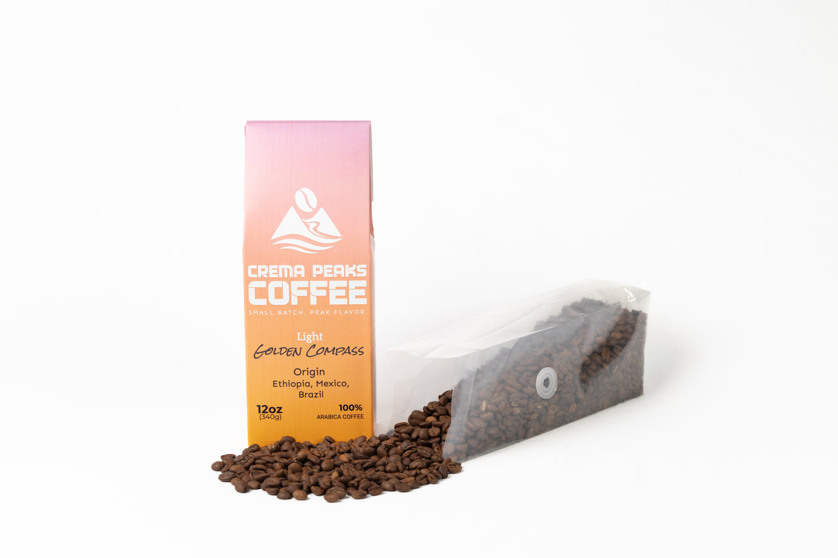 A 12 oz bag of Crema Peaks Coffee Golden Compass on a white background, shown next to spilled coffee beans.