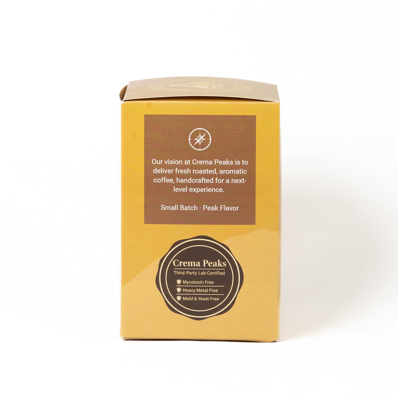 A small rectangular cardboard box for Crema Peaks coffee, shown on a plain white studio background. The box is tan and brown with printed text and a circular logo badge, third-party tested near the bottom.