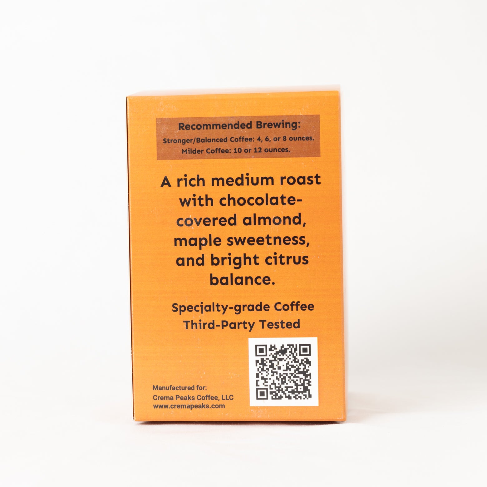 The back of an orange coffee box on a white background, featuring brewing recommendations, product description, a QR code, and the brand name Crema Peaks Coffee, LLC.