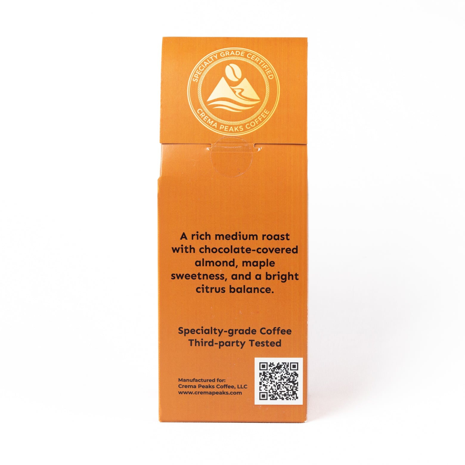 An orange cardboard box for Crema Peaks Coffee, showing the back side with product description text, a circular logo, and a QR code on a white background.