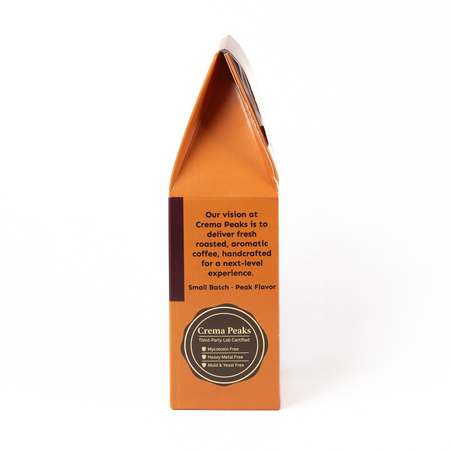 A tall, narrow orange coffee bag package standing upright on a white background, with black text and a circular black label near the bottom. The visible brand on the label is Crema Peaks.
