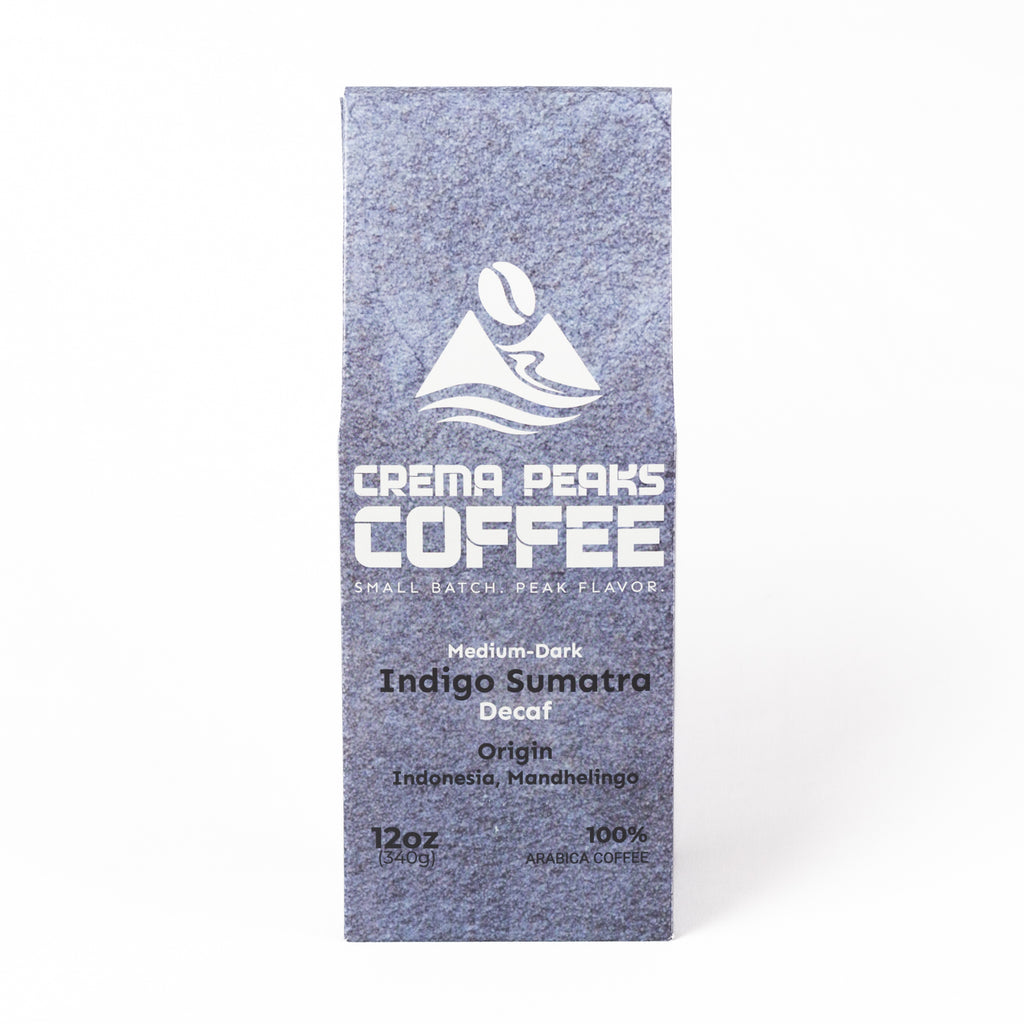 A tall, narrow coffee bag from Crema Peaks Coffee in the Indigo Sumatra Decaf coffee, featuring a textured slate-blue design with white text and logo, set against a plain white background.