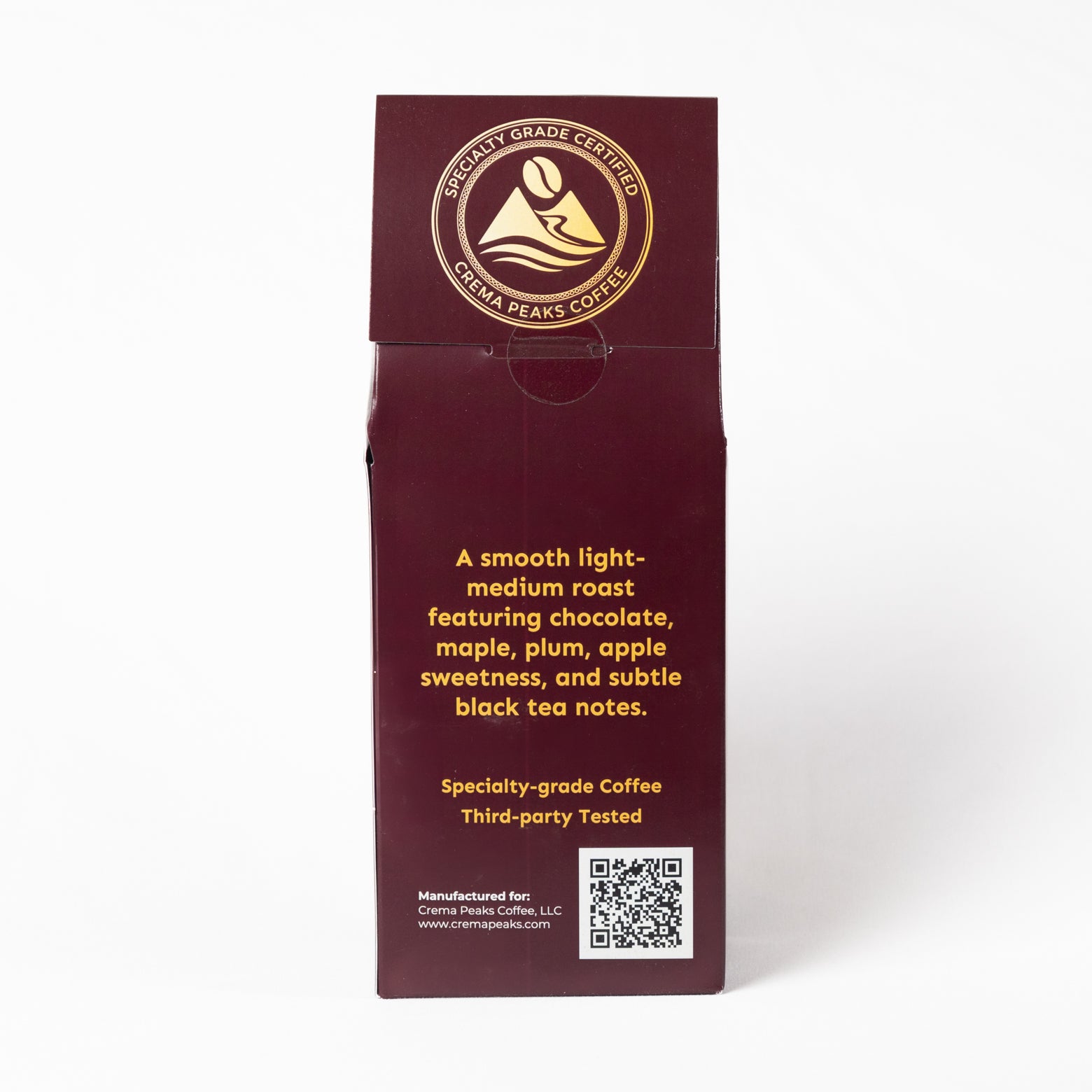 A tall, dark burgundy coffee bag with gold text and logo, photographed upright against a clean white background. The front features the circular 'Crema Peaks Coffee' logo and descriptive text for a specialty-grade light-medium roast coffee.