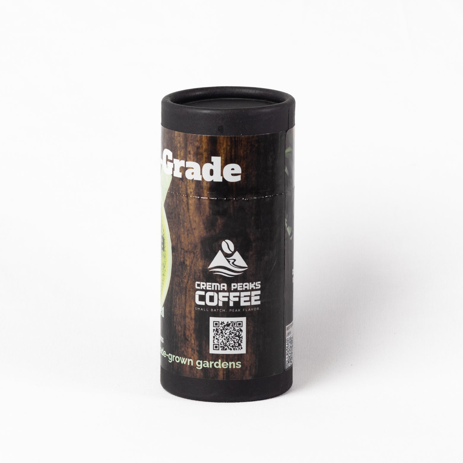 A cylindrical black container of Crema Peaks Coffee Grade, featuring a dark wood-grain label with white text and a logo, set against a plain white background.