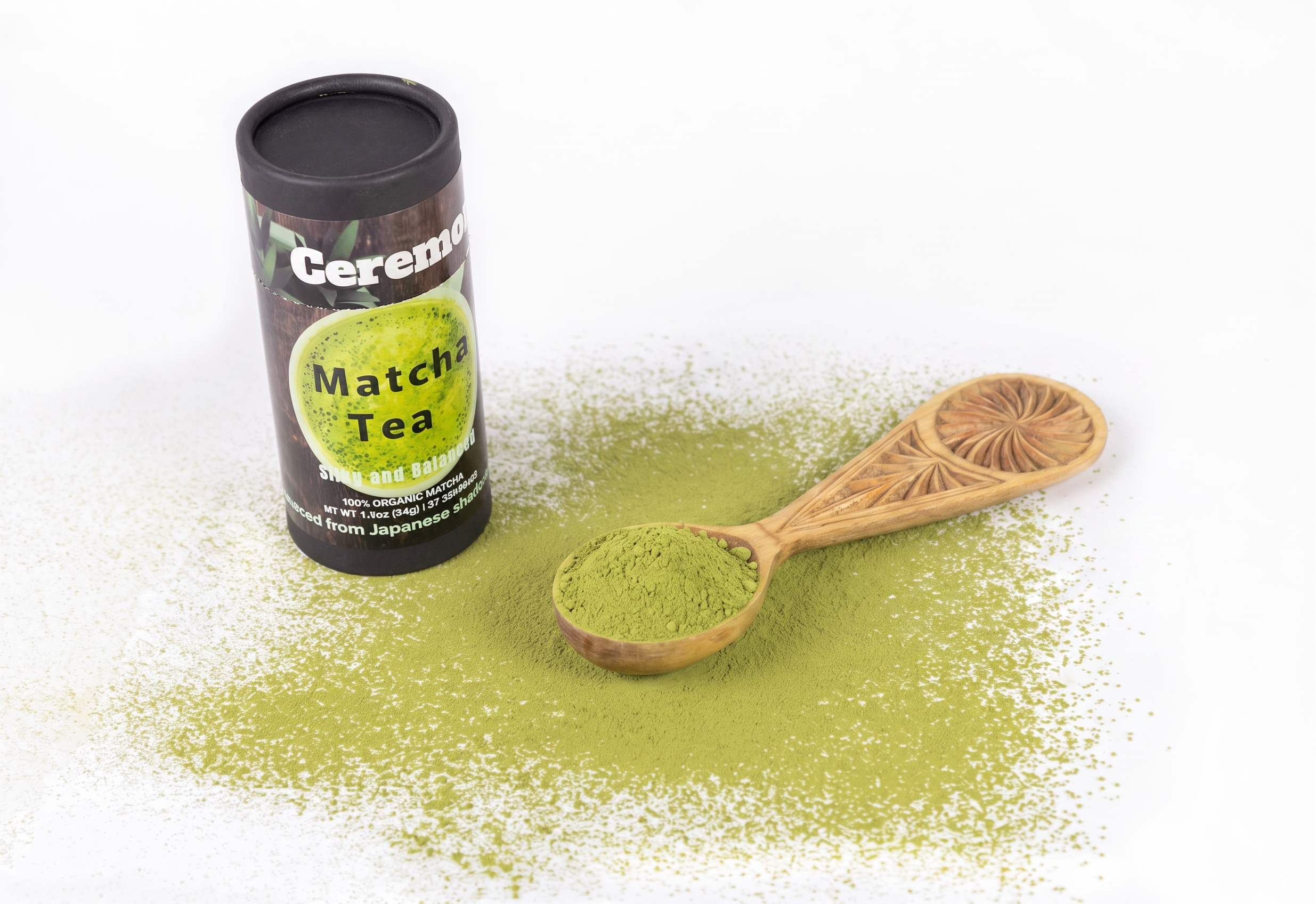 Organic Ceremonial Matcha Tea loose leaf packaging shown next to a wooden spoon filled with green matcha powder and a scattered pile of matcha on a white background.