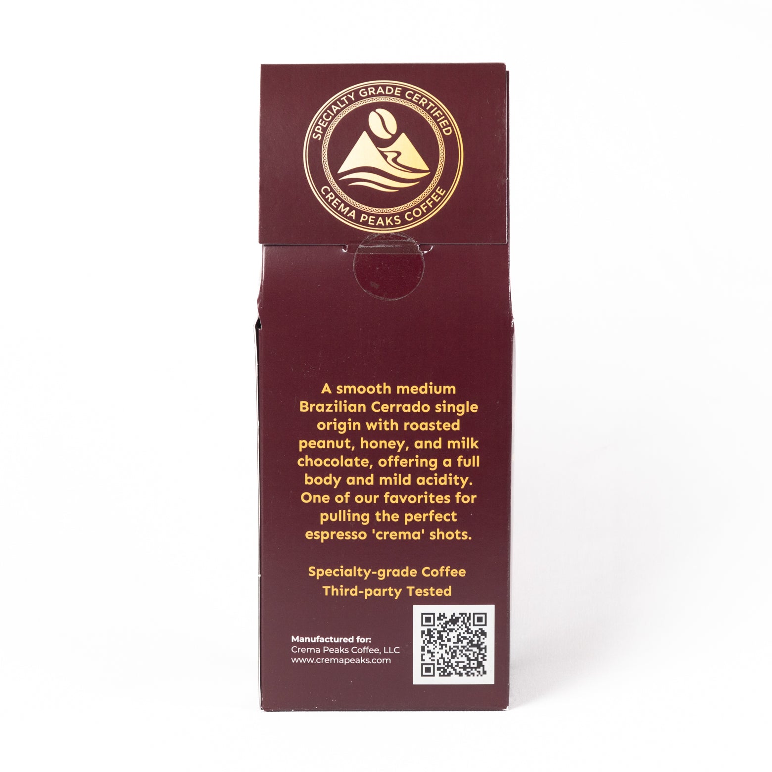 A tall, narrow dark burgundy coffee box shown upright on a white background, with gold text and a circular certified specialty-grade Coffee badge near the top. The front includes descriptive copy about a smooth medium Brazilian Cerrado single-origin coffee and a QR code near the bottom.