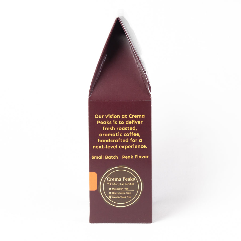 A tall, narrow cream-colored paperboard box shown from the back side, featuring yellow text and a circular gold and white logo for Crema Peaks on a plain white background.