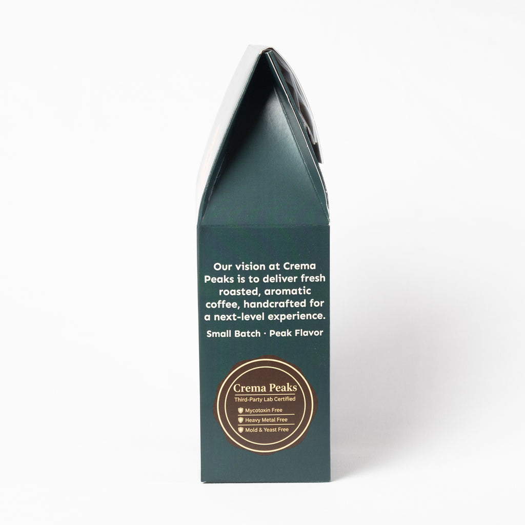 A tall, dark green coffee box shown from the back, featuring white descriptive text and a circular gold logo for Crema Peaks on a clean white background.