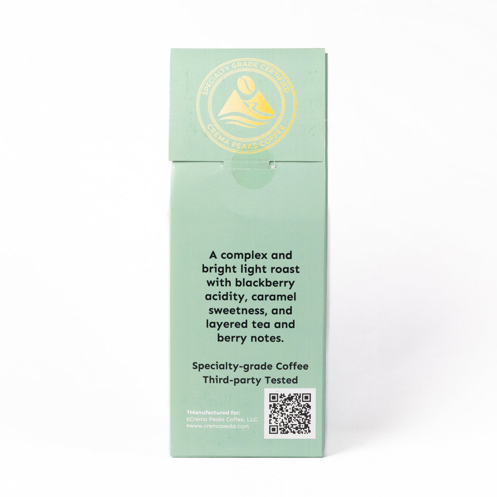 A tall, narrow mint green box for 'Mountain Rose Specialty Coffee' on a clean white background. The box features a gold circular logo at the top and black descriptive text for a specialty-grade coffee with blackberry acidity, caramel sweetness, and layered tea and berry notes.