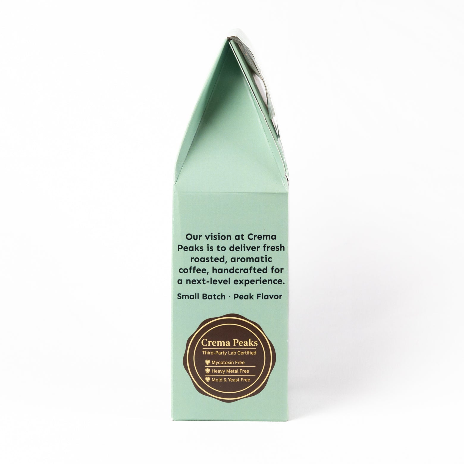 The back panel of a mint green paperboard coffee bag package by Crema Peaks, featuring black descriptive text and a brown circular logo seal on a white background.