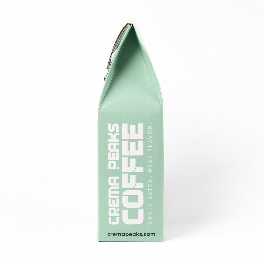A mint green coffee bag package from Crema Peaks Coffee, shown upright against a clean white background. The packaging features bold white text reading 'CREMA PEAKS COFFEE' and smaller text 'SMALL BATCH PEAK FLAVOR.